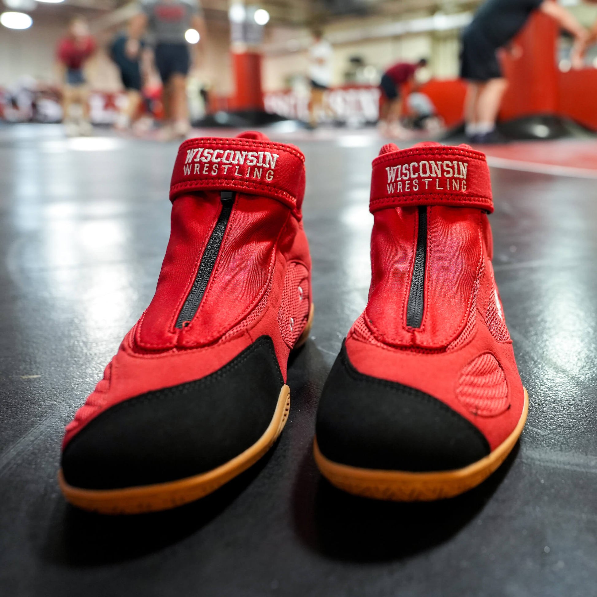 Front-facing view of a pair of red CH Gear Wisconsin Wrestling shoes with ankle straps and zippered lace covers sitting on a wrestling mat.