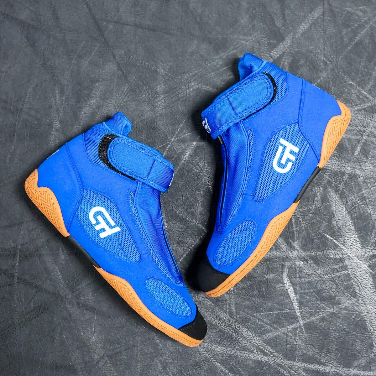 A pair of bright blue high-top athletic CH Gear XXVI Sonic Shoes with orange soles and black toe caps, laid flat on a textured gray surface. Each shoe features a hook-and-loop strap closure and a stylized white logo on the side.